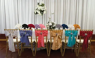 A row of chairs with different colored bows on them.