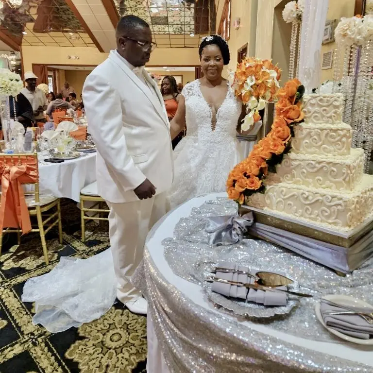 A couple standing in front of a table with cakes on it.