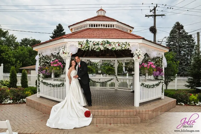 A bride and groom pose for a picture in front of the gazebo.