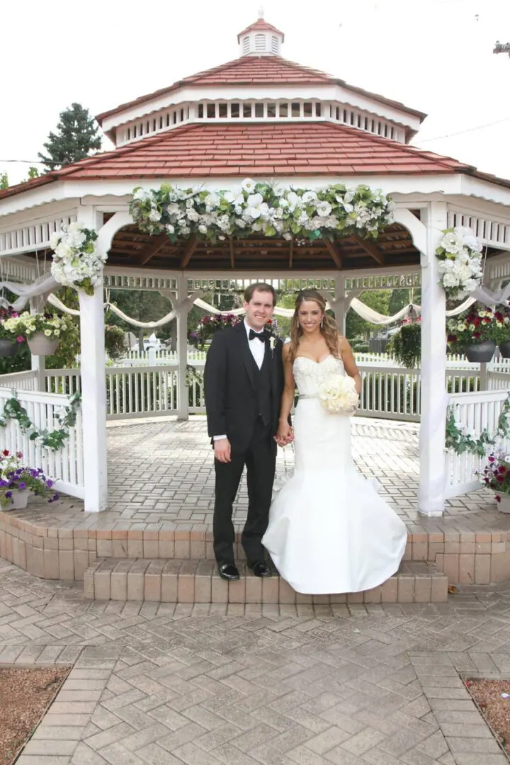 A newly married couple pose for the camera in front of a gazebo.