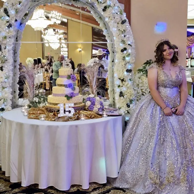 A woman in a ball gown standing next to a cake.