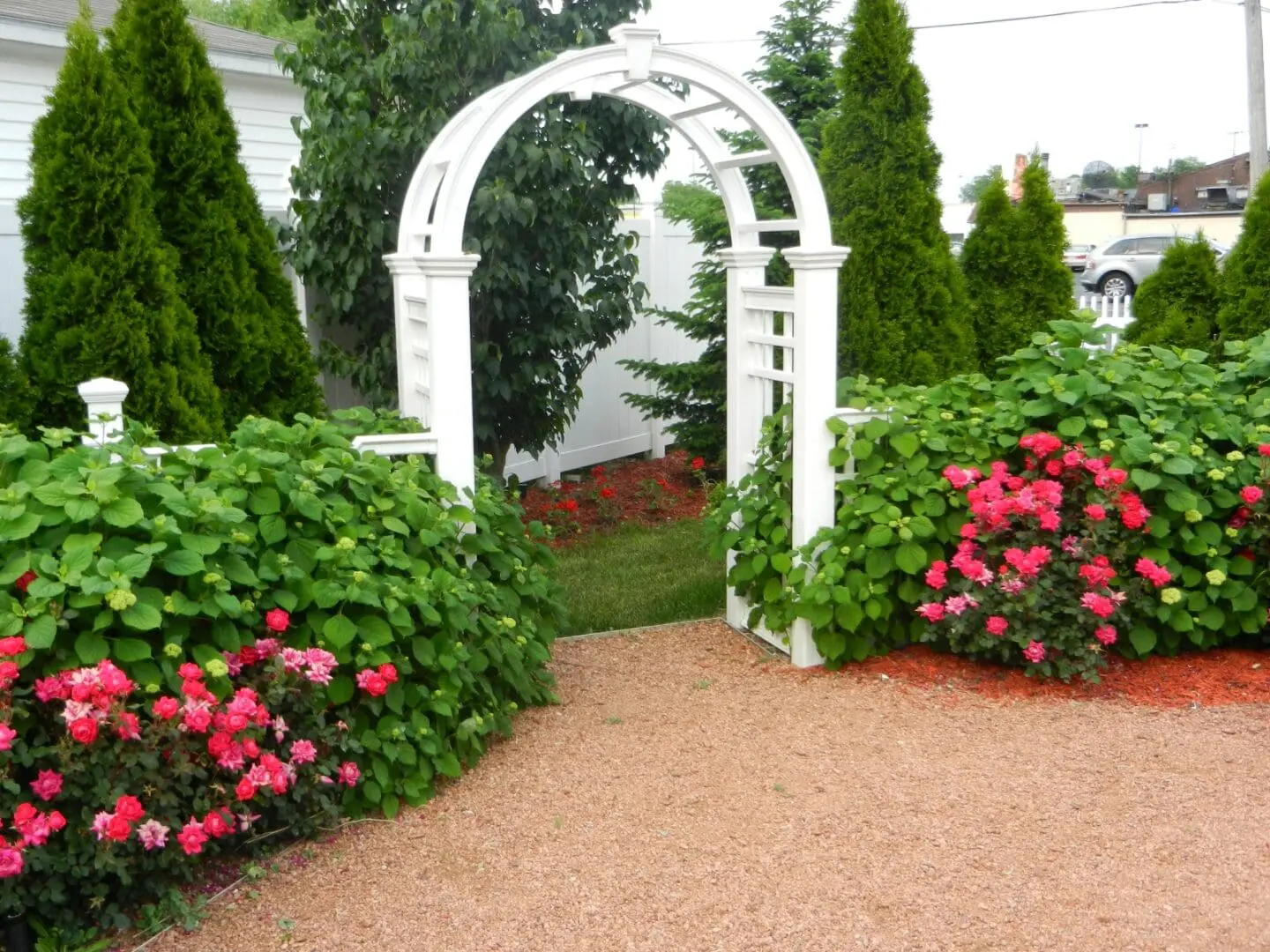 A white arbor in the middle of a garden.